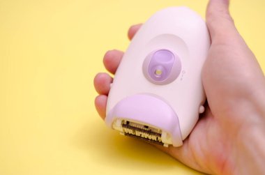 Sarı arka planda beyaz bir epilatör. Erkek eli epilator tutuyor. Saç çıkarma konsepti.