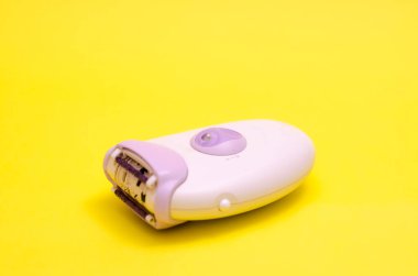 Sarı arka planda beyaz bir epilatör. Saç çıkarma konsepti.