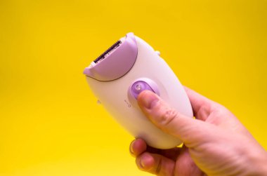Sarı arka planda beyaz bir epilatör. Erkek eli epilator tutuyor. Saç çıkarma konsepti.