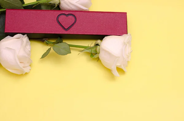 Roses and a gift on a yellow background. Gift wrap with a heart. Place for your text. Love background