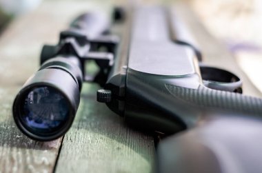 Keskin nişancı tüfeği tahta bir arka planda durur. Optik görüş, yakın plan. Avlanma kavramı.