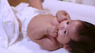 4k Asyalı küçük bebek bebek evde duş aldıktan sonra beyaz bir masaya uzanıyor, mutlu, floresan ışık, gündüz vakti, saf masumiyet, bebek bakımı, bakım, ebeveynlik, hijyen terapisi, evde bakım.
