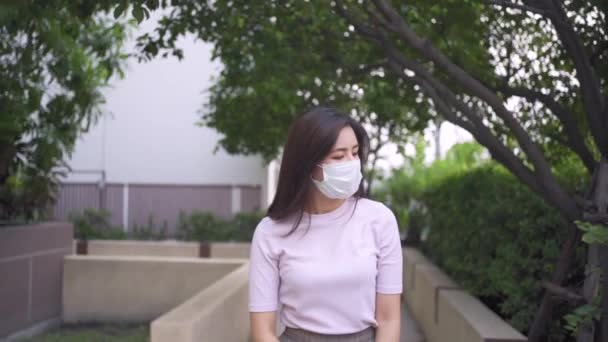 ゆっくりとした動き若いアジアの女性は木の下の地元の住居の歩道を歩くマスクを身に着けています 自己隔離 Covid19コロナウイルス ウイルス拡散防止 カメラフロントビュー 1080P — ストック動画