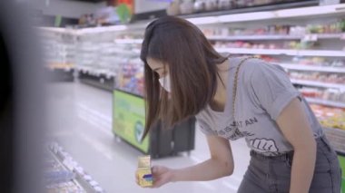 Tıbbi maskeli genç Asyalı kadın süpermarkete alışverişe gidiyor, yiyecek stokluyor, covid19 Corona virüs salgını sırasında yaşam tarzı, sağlıklı seçim iyi seçim, dünya salgını, en iyi raf.