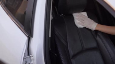 Beyaz eldivenler araba koltuğunu dezenfekte ediyor, temiz sıvıyı beyaz kumaşa püskürtüyor, arabanın içini siliyor, COVID19 Corona virüsünü önlüyor, siyah deri koltuk, hijyen temizliği kirlenmiş yüzey .