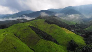 4k açılı insansız hava aracı büyük yeşil dağın, yüksek irtifanın, sisli, bulutların arasından geçen güneş ışığı, soğuk ve serin hava, kış yağmuru mevsimi, tropikal iklim