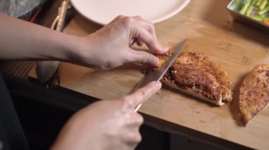 Slow Motion 'da çalışan kadınlar büyük tavuk bifteğini ahşap kesim tahtasında dilimliyor. Mutfak malzemeleri, baharat, yemek pişirme, gizli tarif mutfağı. Omzundan vurulmuş.