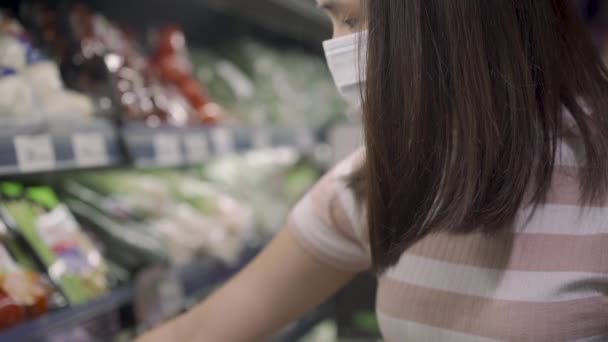 スローモーション若いアジアの女性は 野菜棚 食料品店 ココイド中のライフスタイルを見て医療用マスクを着用19コロナウイルスパンデミック 家庭料理の準備 食料供給の備蓄 — ストック動画