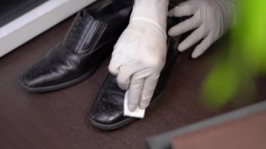 4k el beyaz koruyucu eldiven giyiyor siyah deri erkek ayakkabıları siliyor, eve bakteri, dezenfektan bezi, bakım, corona virüsü covid-19 yayılıyor, mikropları öldürüyor, sağlık hizmetleri, dezenfektan bezi alıyor.
