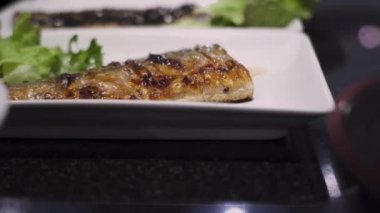 4k Japon tarifi seti menüsü, öğle yemeği zamanı, ızgara balık uskumrusunu beyaz tabakta kapayın, ev yemeği, vitamin omega üç, floresan ışık, siyah masa, yeşil sebze, sol kaydırak, doğu yemeği.