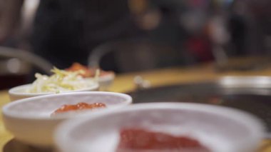 Asya mezesini kapatın ve arka planda bulanık Kore restoranı, Kore usulü ızgara, beyaz tabak, ahşap masa görüntüsü, sağlıklı beslenme, baharatlı lezzetli yemekler, arka planda bulanık insanlar, dışarıda yemek yiyor.