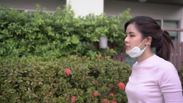 Young Asian Woman Put Mask While Walking Green Palnt Bushes — Vídeo de Stock