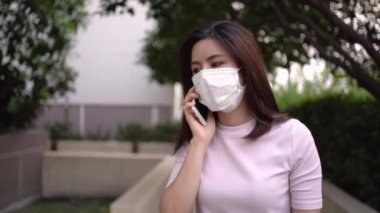 4K Asyalı genç kadın telefon görüşmesi yaparken ve yürürken maske takıyor, ciddi bir konu sorunu, hastalıklardan, sosyal sorunlardan, solunum hastalığından, park dışında yaşam alanının dışında