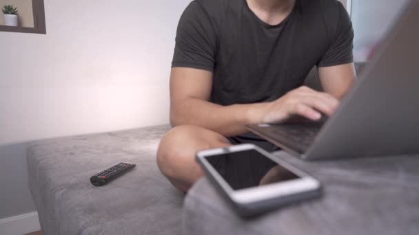 Hombre Asiático Sentado Sofá Usando Ordenador Portátil Con Teléfono Inteligente — Vídeos de Stock