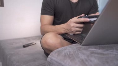 Asyalı adam oyunu oynarken keyif kontrolü ve dizüstü bilgisayar kullanarak evdeki koltukta oturur, teknoloji ve boş zaman, heyecanlı oyuncu joystick 'i tutar, covid-19 salgını sırasında ev karantinası yaşam tarzı, e-spor