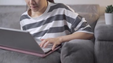 Evde dizüstü bilgisayarla çalışan 4K 'lı genç Asyalı kadın. Kanepede oturup ders çalışmak, serbest çalışmak, ev işleri. Kişisel karantina covid-19, Asyalı üniversite öğrencisi arkadaşlarıyla e-posta sohbeti