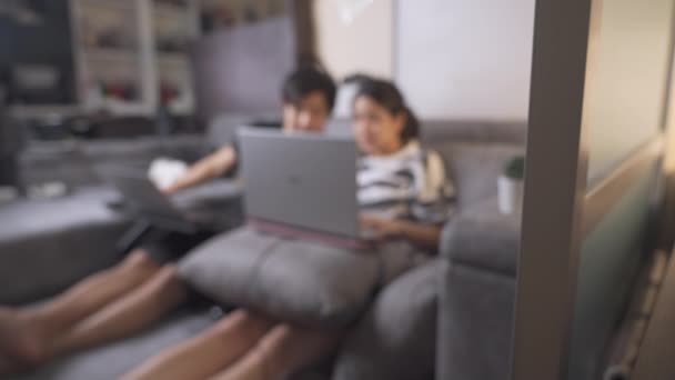 蓝色背景亚洲夫妇坐在灰色的沙发上互相帮助 在客厅的公寓里工作 在家庭隔离期间生活 讨论项目 共同的目标 忙碌的夜晚4K — 图库视频影像
