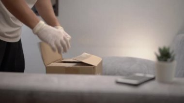Asyalı erkek paketleri boşaltıyor yiyecek kutusu, market alışverişi Corona virüsü sırasında online teslimat servisi covid19, evdeki gri koltukta, karton paketleri açıyor, sebze tedarik ediyor., 
