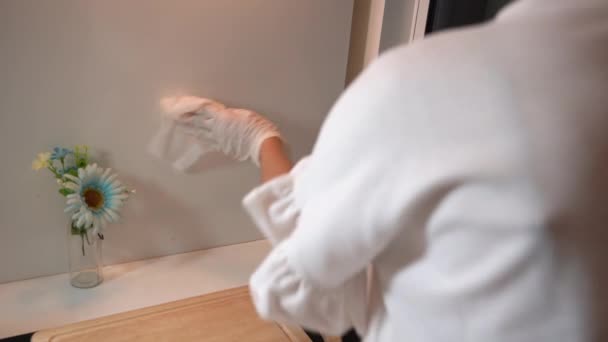 白い手袋の女性は 顔のマスクを着用し 噴霧し 拭くことによってキッチンの壁を消毒し ウイルスが拡散し 汚染された表面 コロナウイルスCovid 家庭用クリーナー 後ろからの眺めを防ぐ — ストック動画
