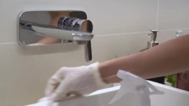 Metalik banyo musluğunu silip temizleyen beyaz eldivenler, temiz servis ürünleri, Corona virüsünü önleyen kovid19, ev temizleme anti bakteri temizleme, mikropları öldürme, kamera yavaşça uzaklaşma.