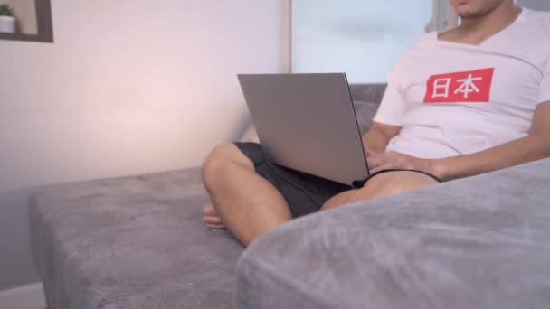 4K中国英语学习网男人穿着白色T恤 用笔记本电脑在家里办公 在自我隔离期间生活方式 甜蜜的家 远程工作的概念 自由职业 在家学习 大学生 放松冷静 — 图库视频影像