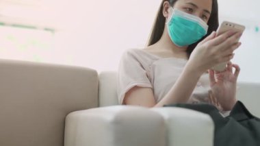 Yeşil maskeli Asyalı çekici bir kadın telefonunu kaydırıyor, akıllı telefon uygulaması kullanıyor, hastalık, sosyal sorunlar, online alışveriş, tıbbi sağlık sorunları, doğal gün ışığı