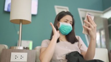 Yeşil maskeli Asyalı kadın akıllı telefondan video görüntüsü alıyor. Yeni normal yaşam tarzı, kovid 19 sırasında karantina ve karantina üzerine video. Sosyal mesafe, video konferans yoluyla konuşan kadın.