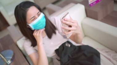 Tıbbi maskeli bir kadın oturmuş video izliyor, yeni normal yaşam tarzı, kovid-19 sırasında arkadaşlarıyla iletişimi koparmıyor, izolasyon ve kendini karantinaya alma videosu çekiyor. Sosyal uzaklık, mutlu aile zamanı.