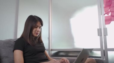 Asyalı genç kadın serbest çalışıyor, gülümsemeyi seviyor kanepeye oturmak, sosyal çalışma mesafesi, kişisel çalışma, online eğitim kursu programı, verimli gün rutini, çevrimiçi sörf 