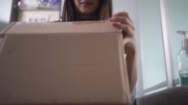 Asyalı bir kadın karton kutuları açıyor, koltukta oturuyor, alıcısı küçük karton paketleri açıyor, covid-19 krizi, paket teslimatı çevrimiçi alışveriş, paketlerin açılması evdeki kanepede oturuyor.