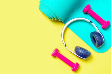 Düz Yat Spor ve Spor Ekipmanı, pembe halterler, kulaklıklar ve sarı arka planda naneli yoga minderi. Metin için boşluk ile yukarıdan görüntüle