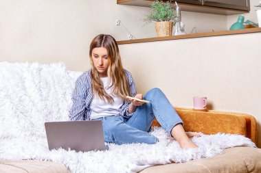 Çevrimiçi eğitim ve çalışma mesafesi. Güzel bir bayan, akıllı telefon kullanıyor, ev ofisinden yatakta çalışıyor ve kahve içiyor. Çevrimiçi dükkanlar ve cep telefonları için bilgisayar kullanmak.