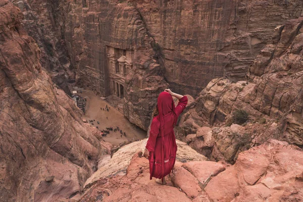 一位身穿红色衣服的女旅行者站在山顶上 向位于约旦 亚洲的佩特拉古城和废墟城的金库眺望 — 图库照片