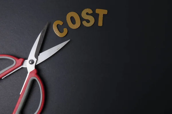 Schaar knipt zakelijke kosten woord kosten om kosten te besparen. Bedrijfsconcept en weinig licht. — Stockfoto