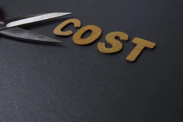 Schaar knipt zakelijke kosten woord kosten om kosten te besparen. Bedrijfsconcept en weinig licht. — Stockfoto