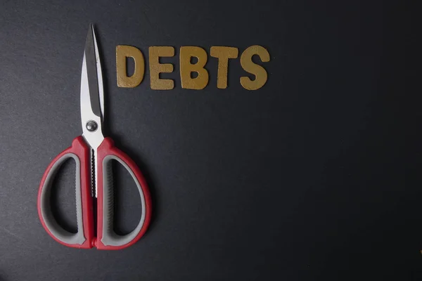 Ножницы и слово DEBTS на черном фоне. Концепция бизнеса — стоковое фото