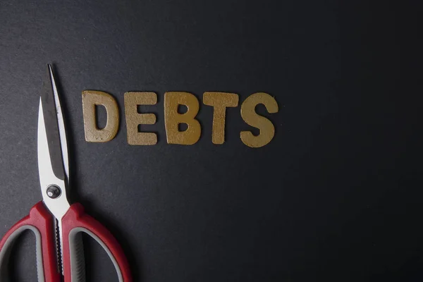 Ножницы и слово DEBTS на черном фоне. Концепция бизнеса — стоковое фото