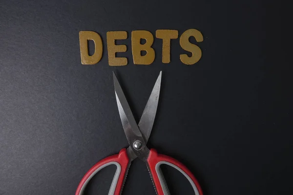 Ножницы и слово DEBTS на черном фоне. Концепция бизнеса — стоковое фото