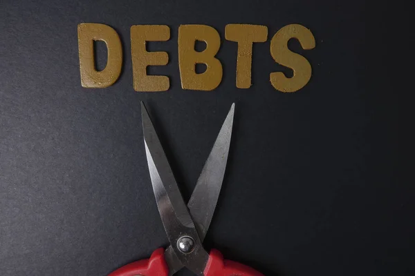 Ножницы и слово DEBTS на черном фоне. Концепция бизнеса — стоковое фото