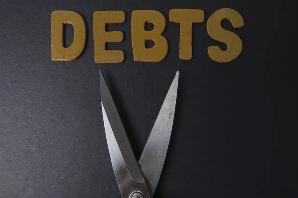 Nożyczki i słowo długów na czarnym tle. Koncepcja biznesowa — Zdjęcie stockowe