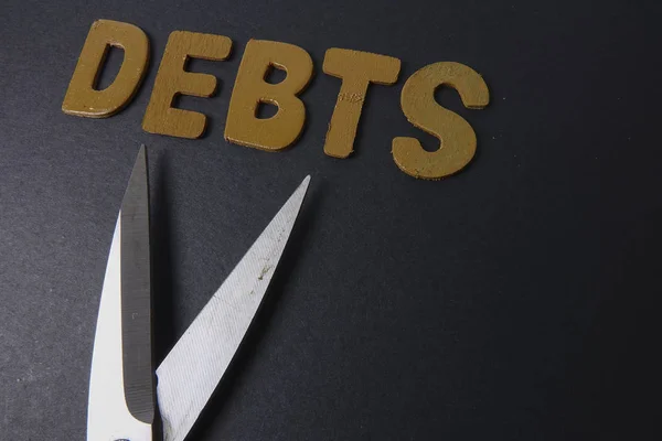 Ножницы и слово DEBTS на черном фоне. Концепция бизнеса — стоковое фото