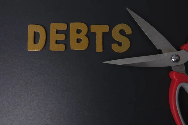 Ножницы и слово DEBTS на черном фоне. Концепция бизнеса — стоковое фото