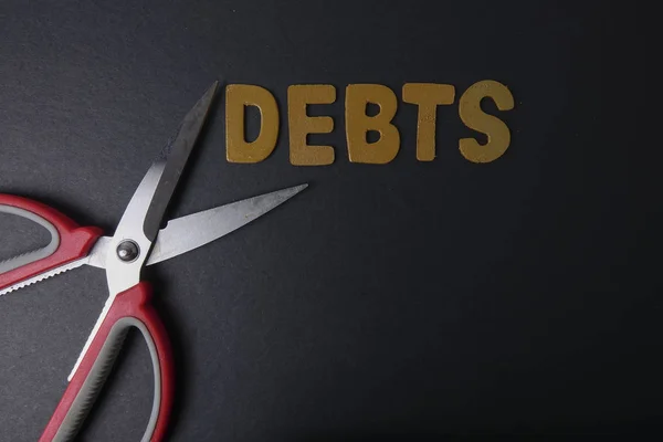 Scissors and word of DEBTS on black background. Business concept