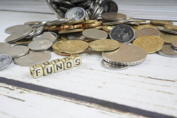 Dice with word FUNDS and coins on wooden background. Funding and business concept. Shallow DOF.