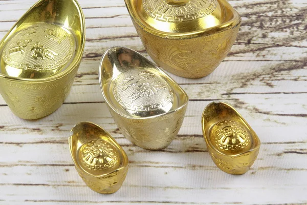 Gold ingots and red money packet for Chinese New Year festive on wooden Background. Chinese character means luck,wealth and prosperity as seen in the image.