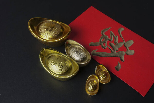 Gold ingots and red money packet for Chinese New Year festive on black background. Chinese character means luck,wealth and prosperity. Low light
