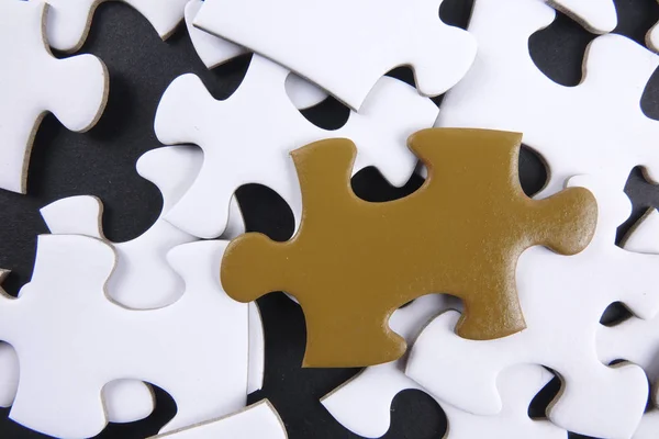 Gold-Puzzle sticht bei weißen Puzzles auf schwarzem Hintergrund hervor. — Stockfoto