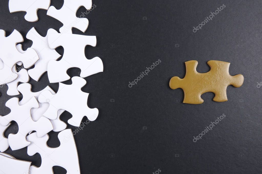 Gold puzzle stand out within white puzzles on black background.