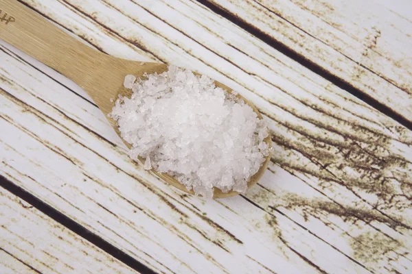 Sea salt in a wooden spoon. Also called bay salt or solar salt, is used in cooking and cosmetics. Rough grained crystals of the mineral.