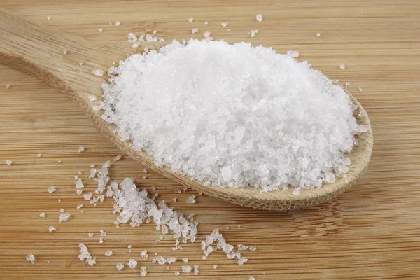 Close up of salt on wooden spoon over wooden background. — Stock Photo, Image